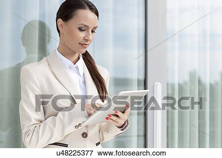 Beautiful businesswoman using digital tablet by glass door View Large Photo Image Stock Photo - Beautiful businesswoman using digital tablet by glass door. Fotosearch