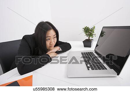 Stock Photo - Bored businesswoman looking at laptop in office. Fotosearch
