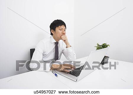Bored mid adult businessman using laptop at desk in office View Large Photo Image Stock Photo - Bored mid adult businessman using laptop at desk in office. Fotosearch