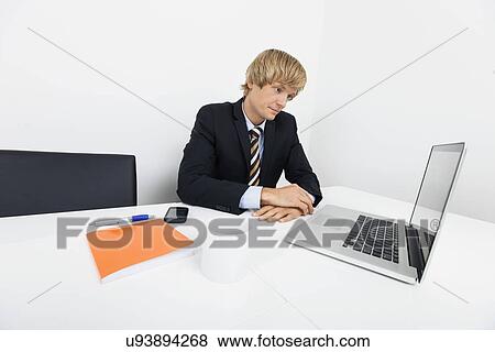 Bored mid adult businessman with laptop at desk in office View Large Photo Image Stock Photo - Bored mid adult businessman with laptop at desk in office. Fotosearch