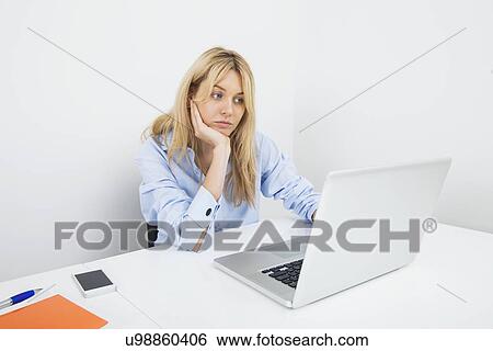 Bored young businesswoman using laptop at desk in office View Large Photo Image Stock Photograph - Bored young businesswoman using laptop at desk in office. Fotosearch