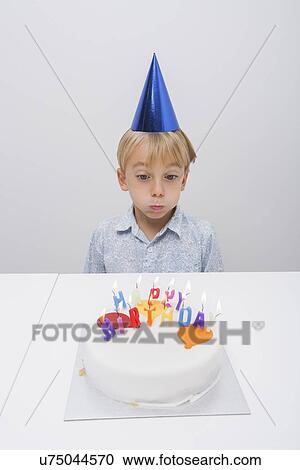 Stock Image - Boy blowing candles on birthday cake at table in house. Fotosearch