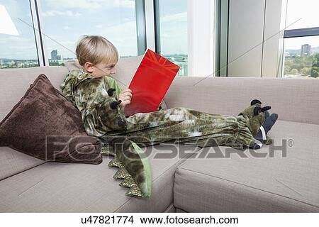Boy in dinosaur costume reading story book on sofa at home View Large Photo Image Picture - Boy in dinosaur costume reading story book on sofa at home. Fotosearch