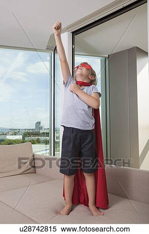 Stock Photography - Boy in pretending to be super hero on sofa bed at home. Fotosearch