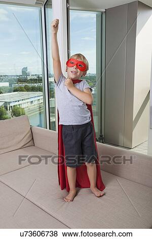 Boy in super hero costume standing with arm raised on sofa bed at home View Large Photo Image Stock Photo - Boy in super hero costume standing with arm raised on sofa bed at home. Fotosearch