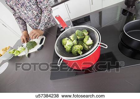 Broccoli in colander on saucepan with man standing at kitchen counter View Large Photo Image Stock Photo - Broccoli in colander on saucepan with man standing at kitchen counter. Fotosearch