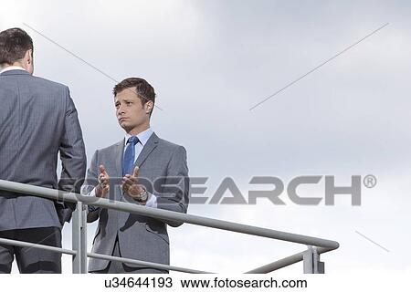 Stock Image - Businessman gesturing while communicating with coworker against sky. Fotosearch