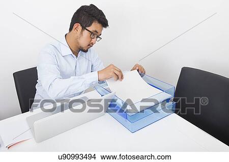 Picture - Businessman searching documents at desk in office. Fotosearch