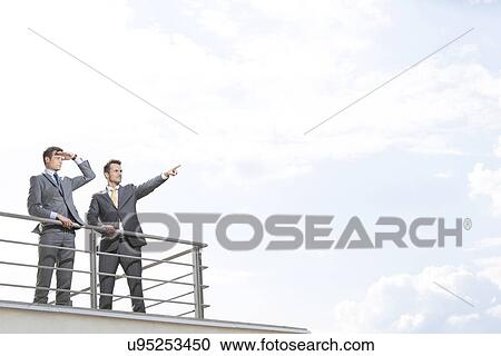 Stock Image - Businessman showing something to coworker against cloudy sky. Fotosearch