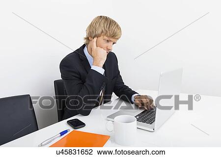 Businessman using laptop at desk in office View Large Photo Image Stock Image - Businessman using laptop at desk in office. Fotosearch