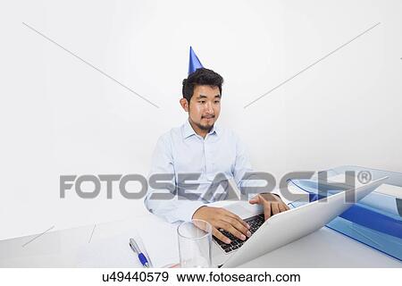 Businessman wearing party hat while using laptop in office View Large Photo Image Stock Photo - Businessman wearing party hat while using laptop in office. Fotosearch