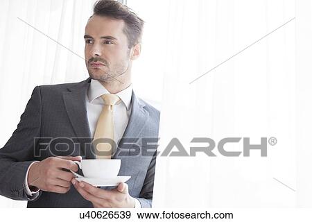 Businessman with coffee cup looking away in office View Large Photo Image Stock Photo - Businessman with coffee cup looking away in office. Fotosearch