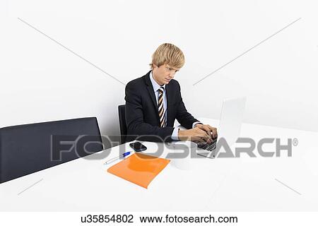 Stock Image - Businessman working on laptop at desk in office. Fotosearch
