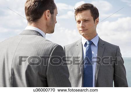 Stock Image - Businessmen looking at each other against sky. Fotosearch