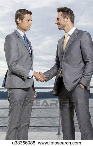 Stock Photography - Businessmen shaking hands on terrace against sky. Fotosearch