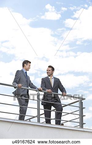Picture - Businessmen standing at terrace railings against sky. Fotosearch