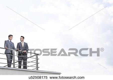 Businessmen standing at terrace railings against cloudy sky View Large Photo Image Stock Photography - Businessmen standing at terrace railings against cloudy sky. Fotosearch