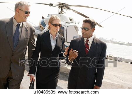Stock Photography - Businesspeople communicating with helicopter in background. Fotosearch