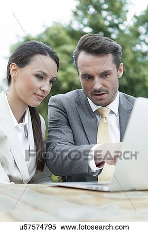 Stock Photography - Businesspeople discussing over laptop outdoors. Fotosearch
