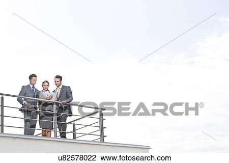 Businesspeople standing at terrace railings against sky View Large Photo Image Stock Image - Businesspeople standing at terrace railings against sky. Fotosearch