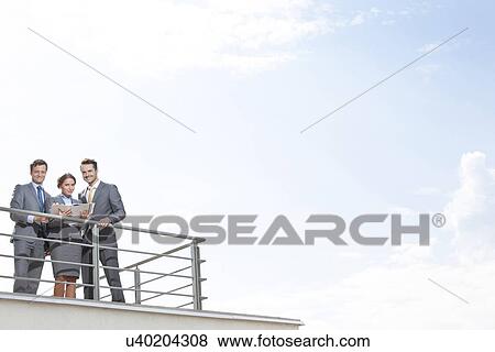 Stock Photo - Businesspeople standing at terrace railings against sky. Fotosearch