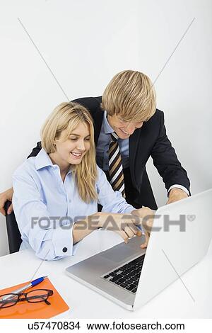 Picture - Businesspeople using laptop at desk in office. Fotosearch