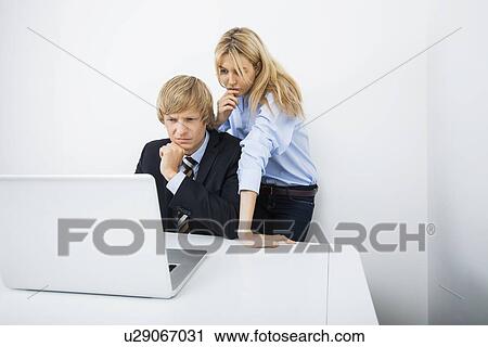 Stock Image - Businesspeople using laptop together at desk in office. Fotosearch
