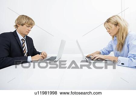 Stock Photo - Businesspeople using laptops at desk in office. Fotosearch