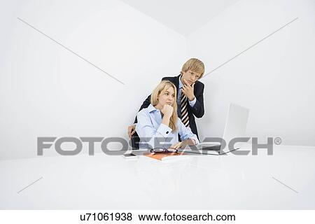Businesspeople with hand on chin looking at laptop in office View Large Photo Image Stock Photo - Businesspeople with hand on chin looking at laptop in office. Fotosearch