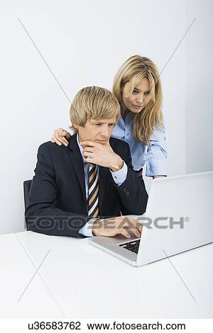 Stock Image - Businesspeople working on laptop at desk in office. Fotosearch