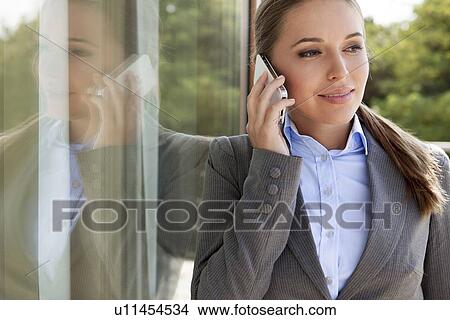 Picture - Businesswoman answering cell phone by glass door. Fotosearch