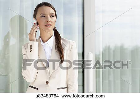 Picture - Businesswoman answering cell phone by glass door. Fotosearch
