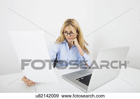 Businesswoman in eyeglasses reading document at office desk View Large Photo Image Stock Photo - Businesswoman in eyeglasses reading document at office desk. Fotosearch