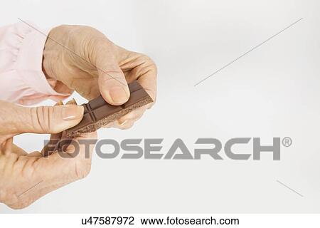 Stock Image - Businesswoman's hands holding chocolate bar in office. Fotosearch