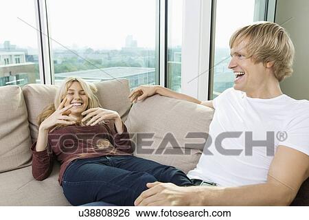 Cheerful couple relaxing on sofa at home View Large Photo Image Stock Photograph - Cheerful couple relaxing on sofa at home. Fotosearch