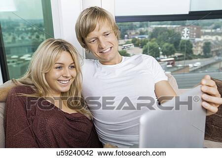 Stock Image - Cheerful couple using laptop in living room at home. Fotosearch