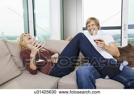 Stock Image - Cheerful relaxed couple with wine glasses in living room at home. Fotosearch