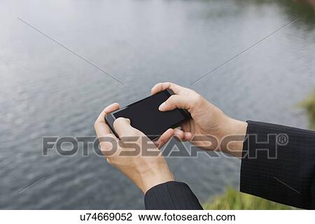 Stock Image - Close-up of businessman's hands texting on smart phone along river. Fotosearch