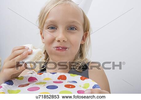 Close-up of cute girl eating birthday cake against gray background View Large Photo Image Stock Image - Close-up of cute girl eating birthday cake against gray background. Fotosearch