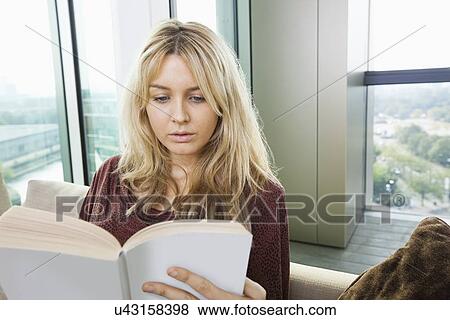 Stock Photo - Close-up of relaxed young woman reading book in living room at home. Fotosearch