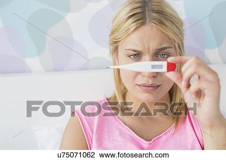 Stock Image - Close-up of sick woman taking temperature with thermometer in bed. Fotosearch