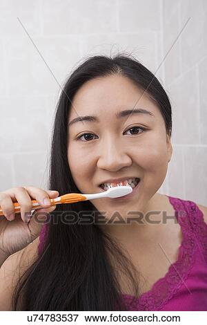 Stock Photo - Close-up view of young Asian woman brushing her teeth in bathroom. Fotosearch