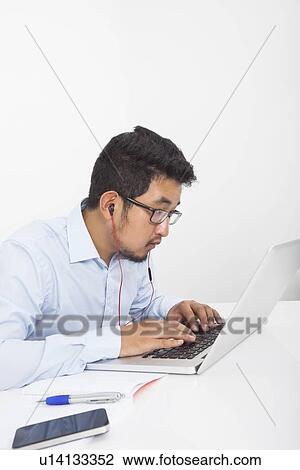 Stock Image - Concentrated businessman using laptop while listening music in office. Fotosearch
