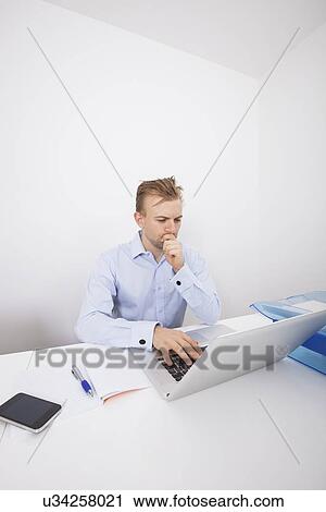 Stock Image - Concentrated businessman using laptop at desk in office. Fotosearch