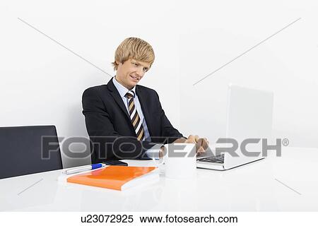 Stock Photography - Confident businessman using laptop at desk in laptop. Fotosearch