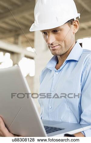 Confident male architect using laptop at construction site View Large Photo Image Stock Photo - Confident male architect using laptop at construction site. Fotosearch