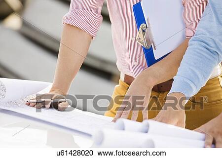 Stock Image - Cropped image of architects with blueprints and clipboard. Fotosearch
