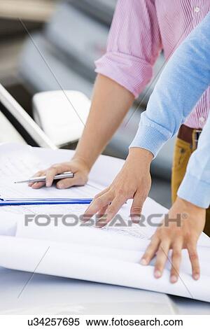 Stock Photography - Cropped image of architects with blueprints on car at site. Fotosearch
