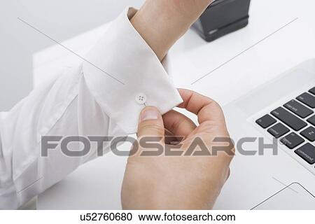 Stock Image - Cropped image of businessman buttoning his cuff in office. Fotosearch