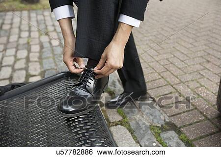 Stock Photograph - Cropped image of businessman tying his shoe on bench. Fotosearch